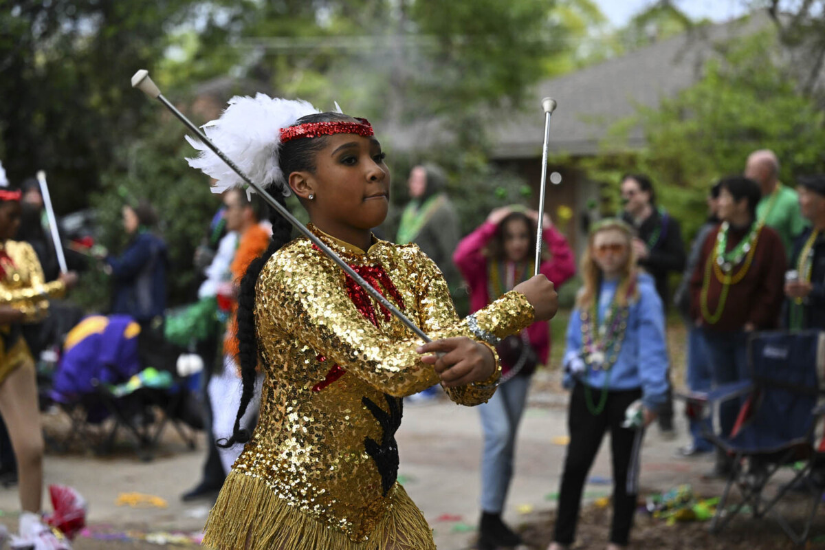 A member of a marching band in a gold costume twirls a set of batons