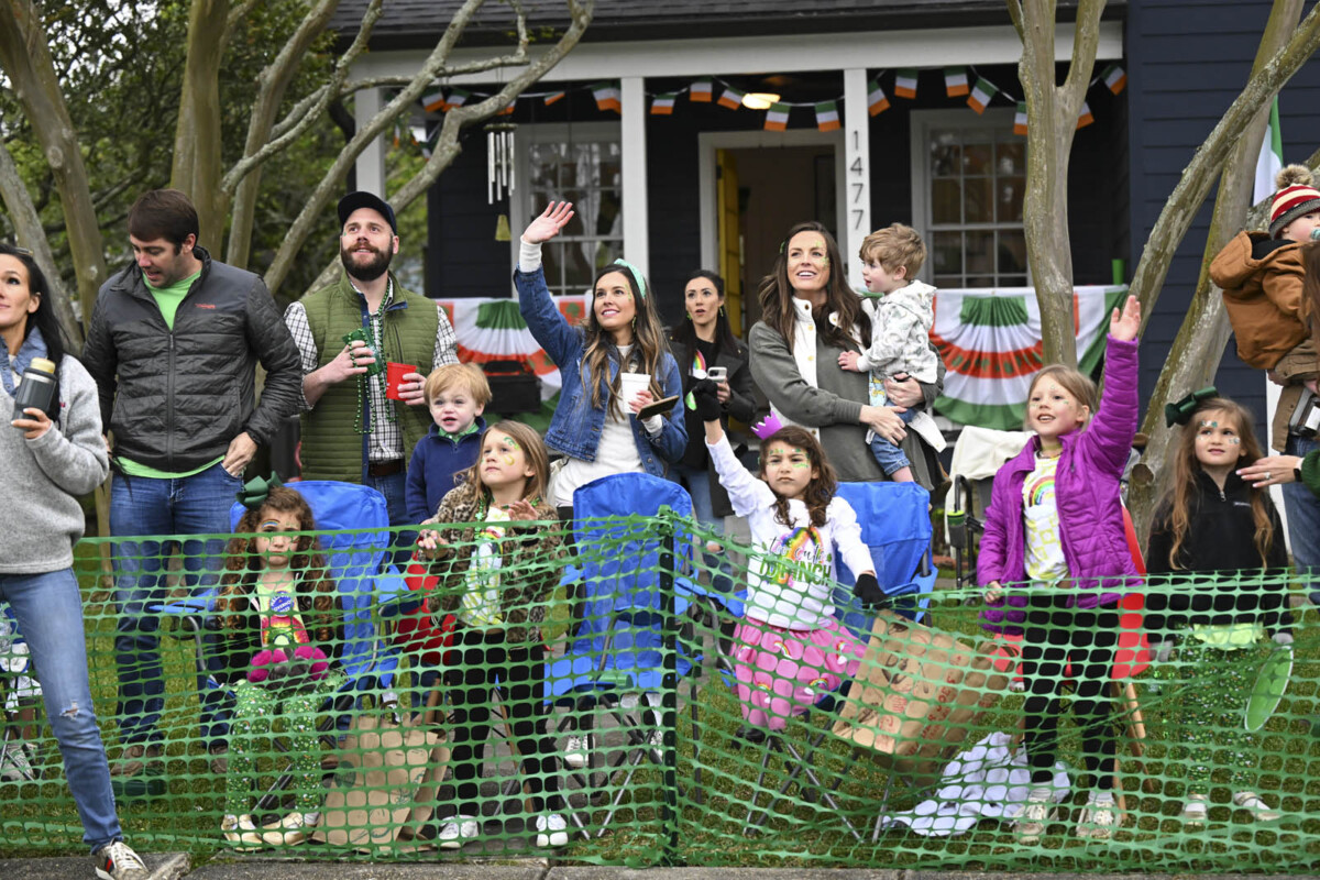 Several families gathered in front of a house catch beads during the Wearin of the Green parade