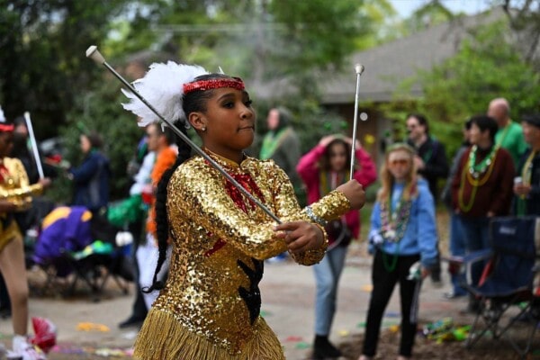 A band member in a gold uniform twirls a couple of batons during the 2023 parade