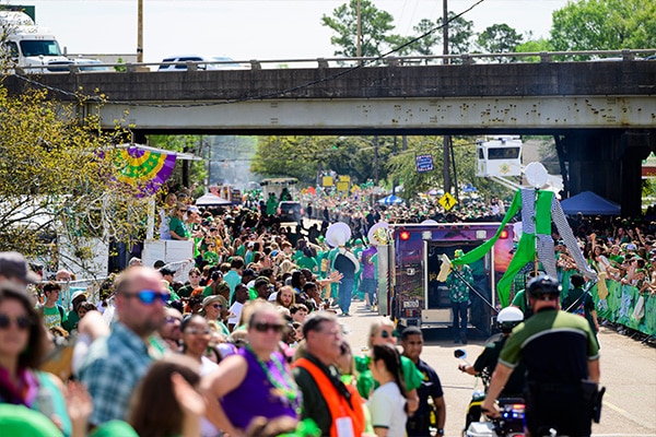 A vibrant 2024 St. Patrick's Day parade filled with people wearing green, with decorations and floats under a sunny sky, celebrates the tradition of Wearin' of the Green.
